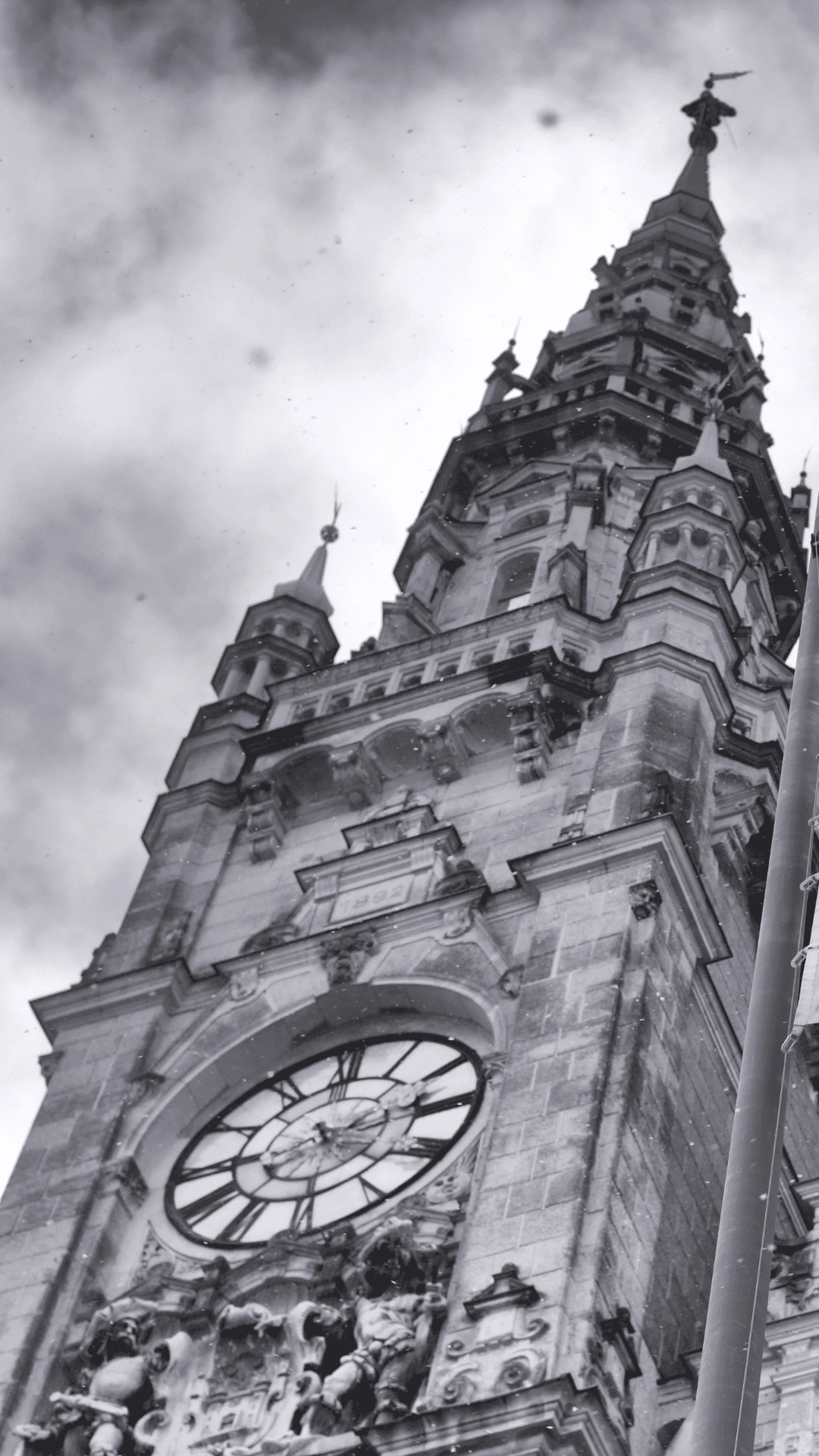Černobílá fotografie věže s hodinami a sochami na historické budově